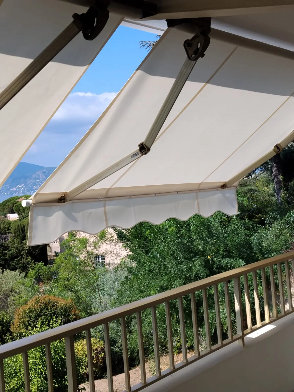 Store banne clair déployé sur un balcon avec vue sur les collines et les jardins.