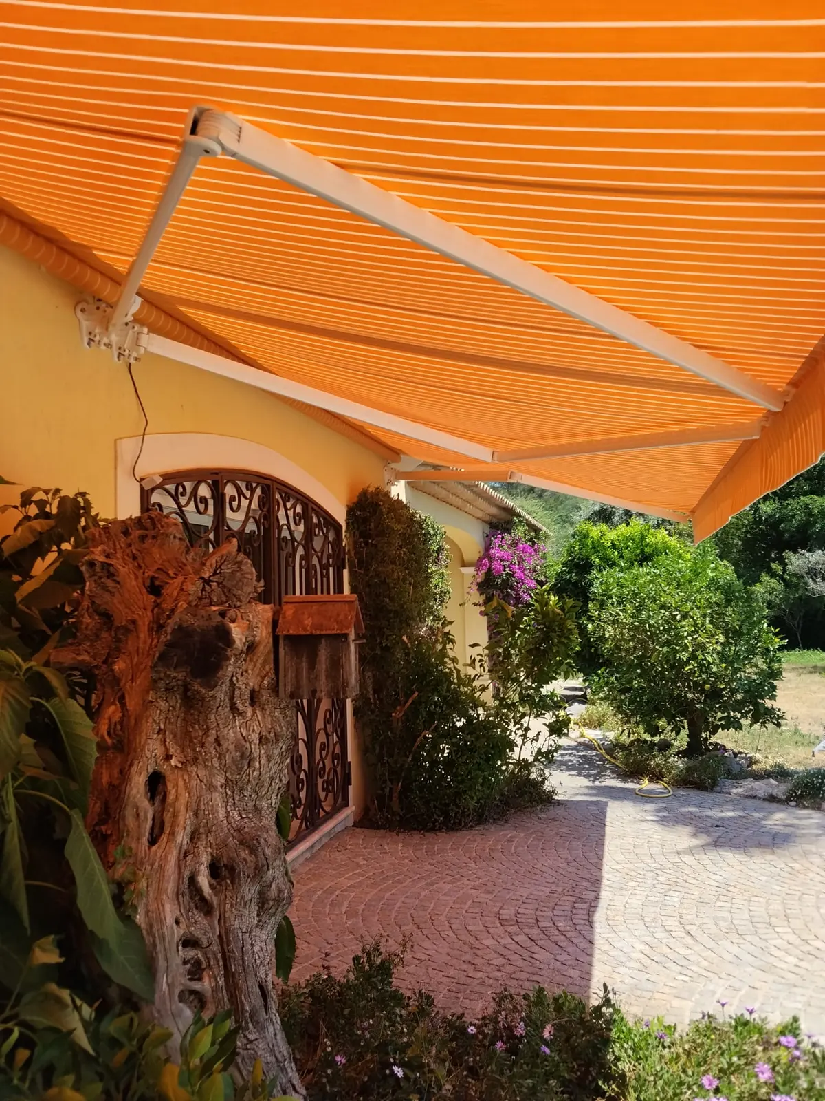 Store banne orange déployé devant une maison et une terrasse arborée.