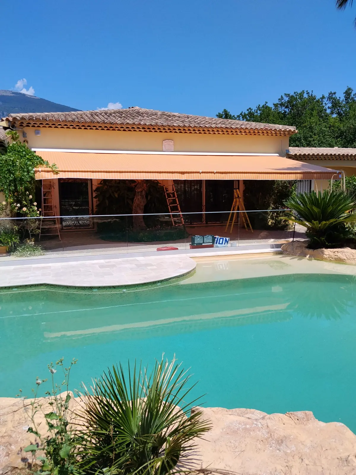 Store banne clair installé au-dessus d’une terrasse et d’une piscine.